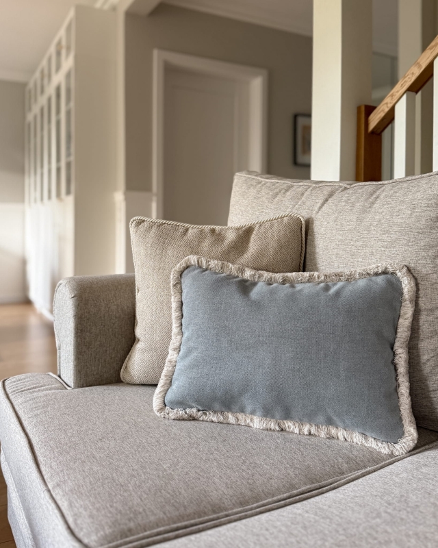 Prostokątna błękitna poduszka z frędzlami GISELLE I w aranżacji poduszek na kanapie.