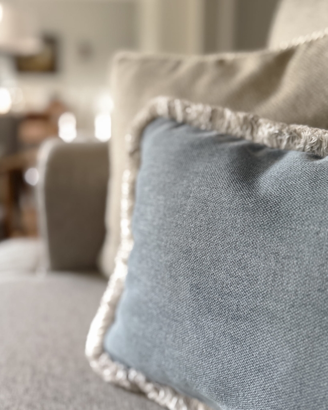 Prostokątna błękitna poduszka z frędzlami GISELLE I w aranżacji poduszek na kanapie - zbliżenie.