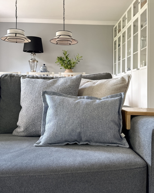 Błękitna poduszka z tkaniny o grubym splocie AZURE - 45x45 cm w aranżacji na kanapie.