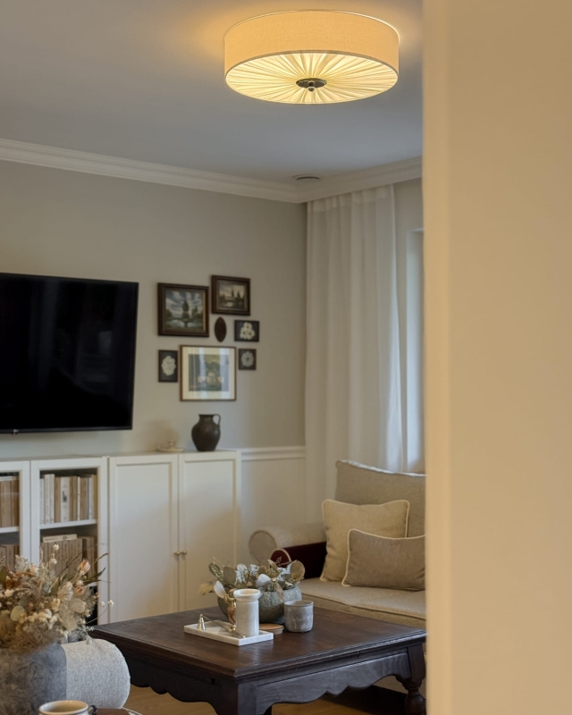 Duża elegancka lampa sufitowa w kolorze złamanej bieli w salonie PLISE BLACK III - zapalone światło.