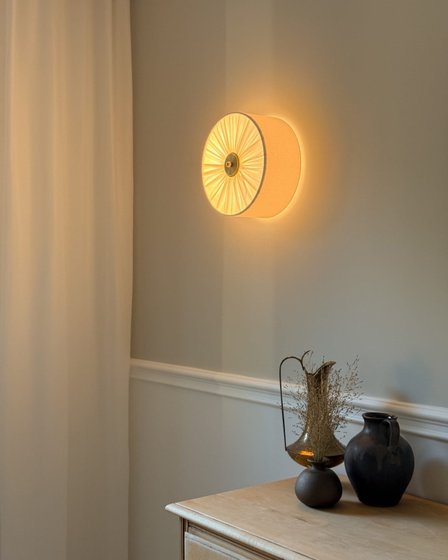 Elegancki kinkiet w kolorze złamanej bieli z mosiężnym dekorem PLISE BRASS I - zapalone światło.