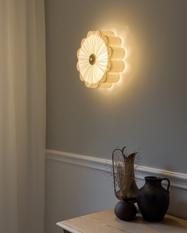 Biały kinkiet w kształcie kwiatu z mosiężnym dekorem PEONIA I śmietankowa biel w aranżacji na ścianie - zapalone światło.
