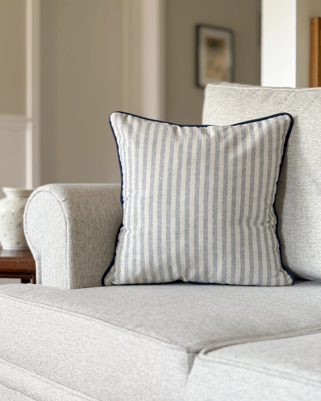 Kwadratowa bawełniana poduszka ozdobna w niebieskie paski na szarobeżowym tle MARINA 45x45 cm - aranżacja na kanapie.