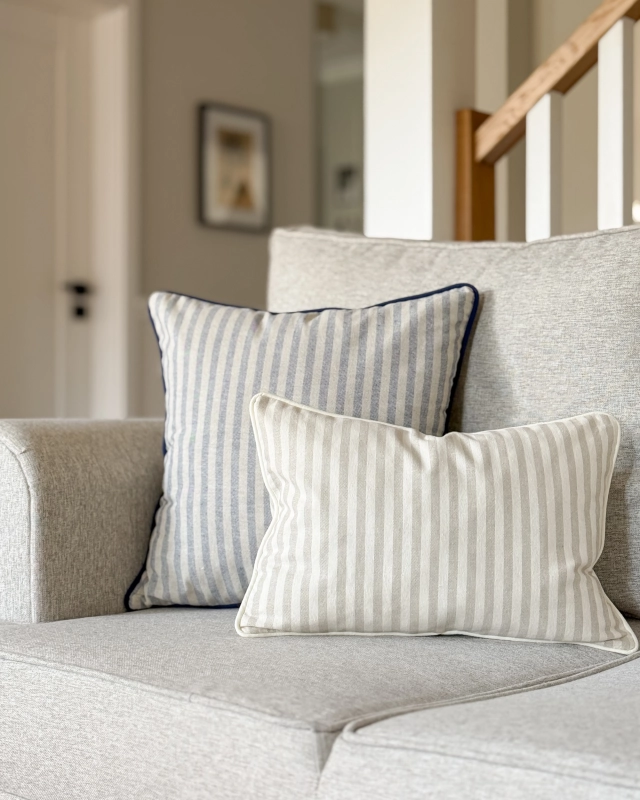 Kwadratowa bawełniana poduszka ozdobna w niebieskie paski na szarobeżowym tle MARINA 45x45 cm - aranżacja na kanapie.