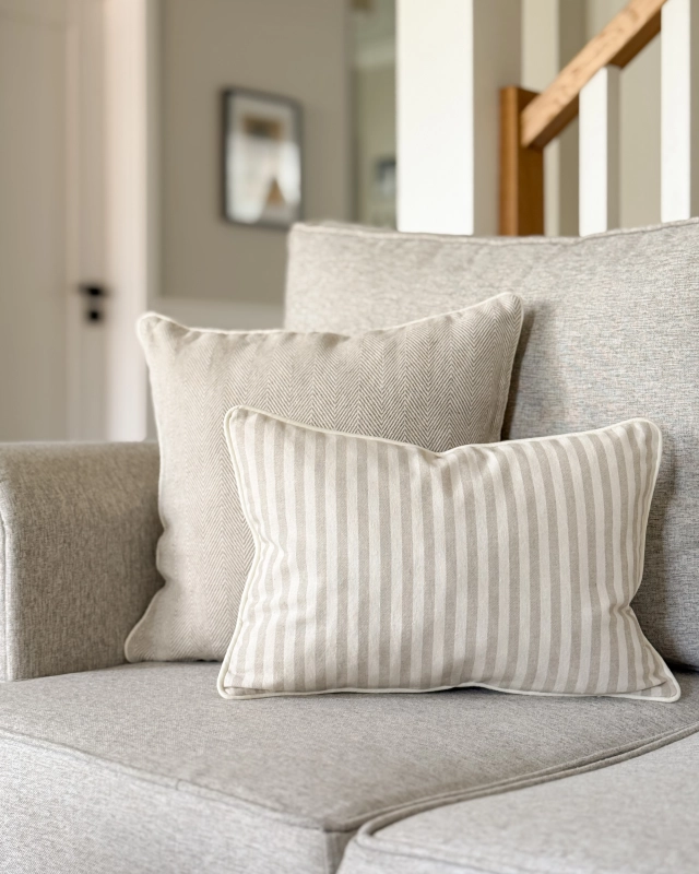 Prostokątna poduszka bawełniana w beżowo-kremowe paski SAND 30x45 cm w aranżacji na kanapie.