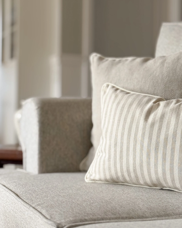 Prostokątna poduszka bawełniana w beżowo-kremowe paski SAND 30x45 cm w aranżacji na kanapie.