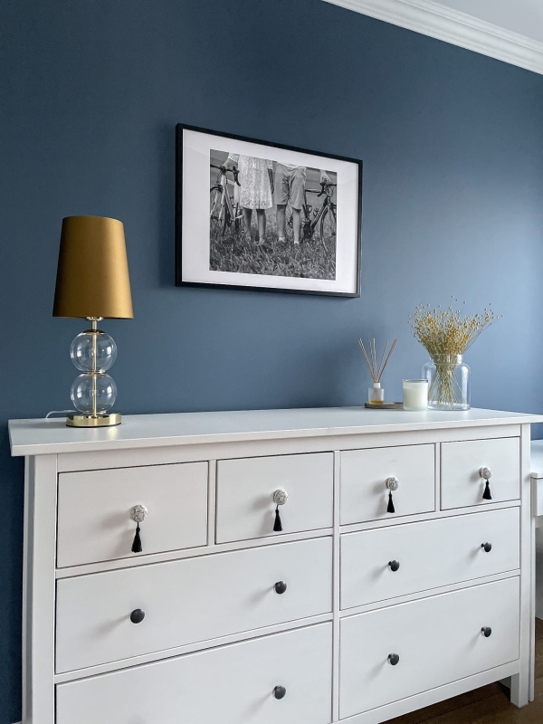 Złota lampka stołowa ze szklanymi elementami i abażurem w kolorze starego złota Kaspa COCO w aranżacji na białej komodzie.