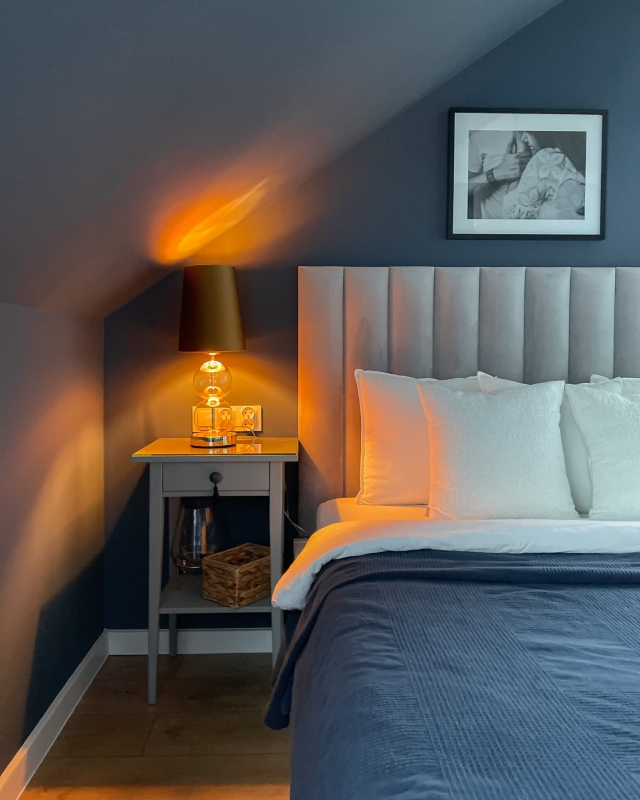 Złota lampka stołowa ze szklanymi elementami i abażurem w kolorze starego złota Kaspa COCO w aranżacji jako lampka nocna w granatowej sypialni.